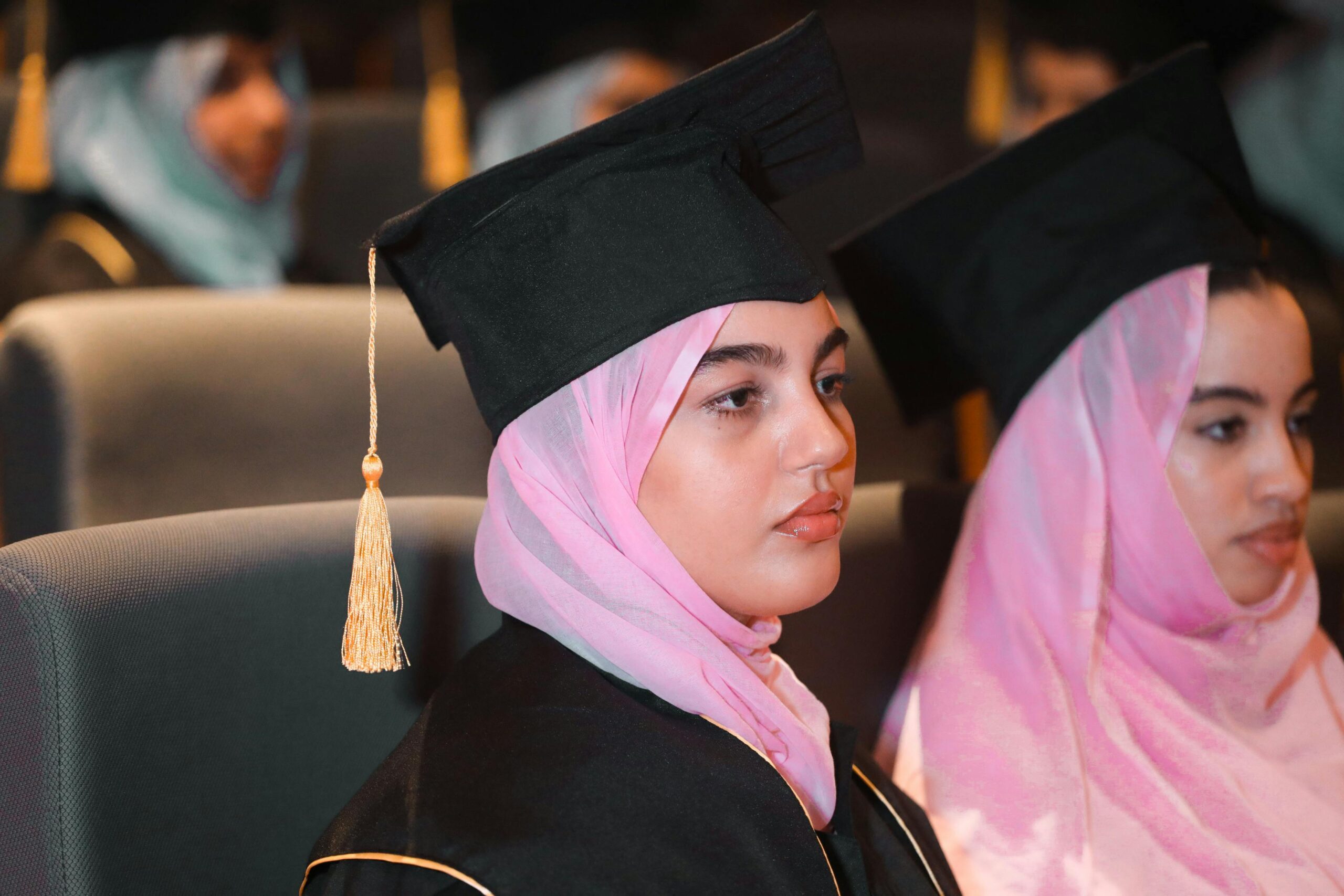 Young women in hijabs and caps at a graduation ceremony, celebrating academic achievements.